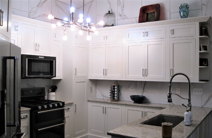 A modern kitchen with marble wall tile, white cabinets, a black gas range and microwave, and a granite countertop with a sink and faucet.
